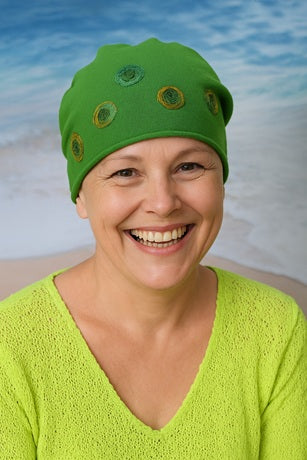 Frau eine leichte handgemachte grüne Baumwollmütze mit dekorativen Spiralapplikationen vor einem Strandhintergrund