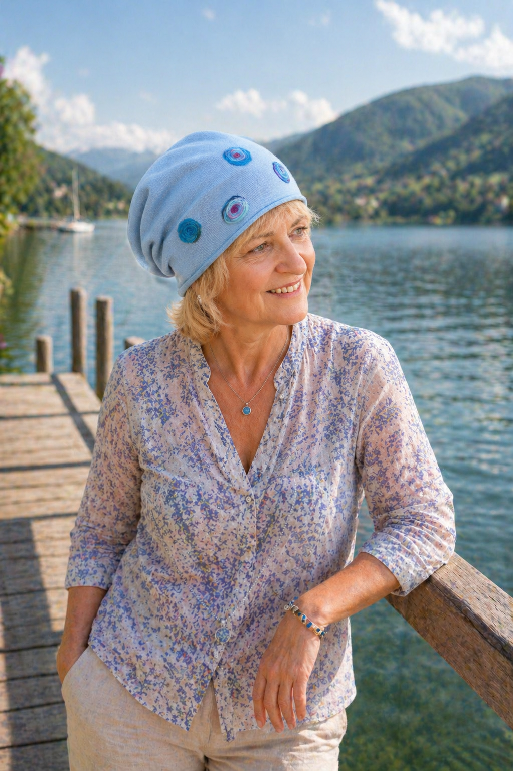 Ältere Frau mit handmade Sommermütze aus Baumwolle steht lächelnd auf einem Steg am See