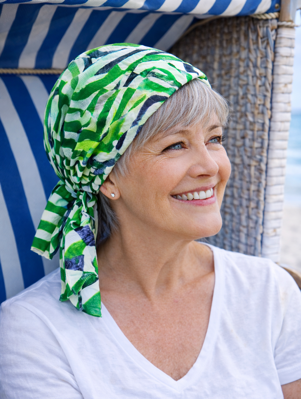 „Reife Frau trägt grün gemustertes Kopftuch aus leichter Baumwolle ohne Binden,sitzt im Strandkorb am Meer“